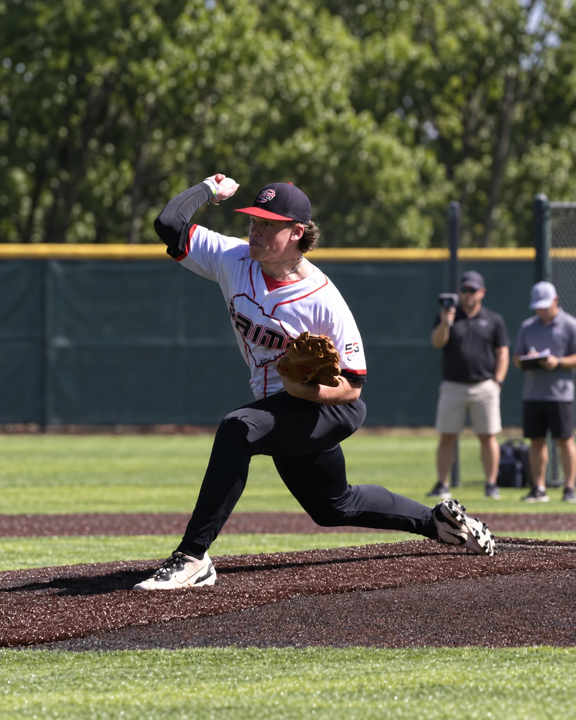 Photo edit of a high-school pitcher in his 5G Prime uniform, with scouts evaluating in the background